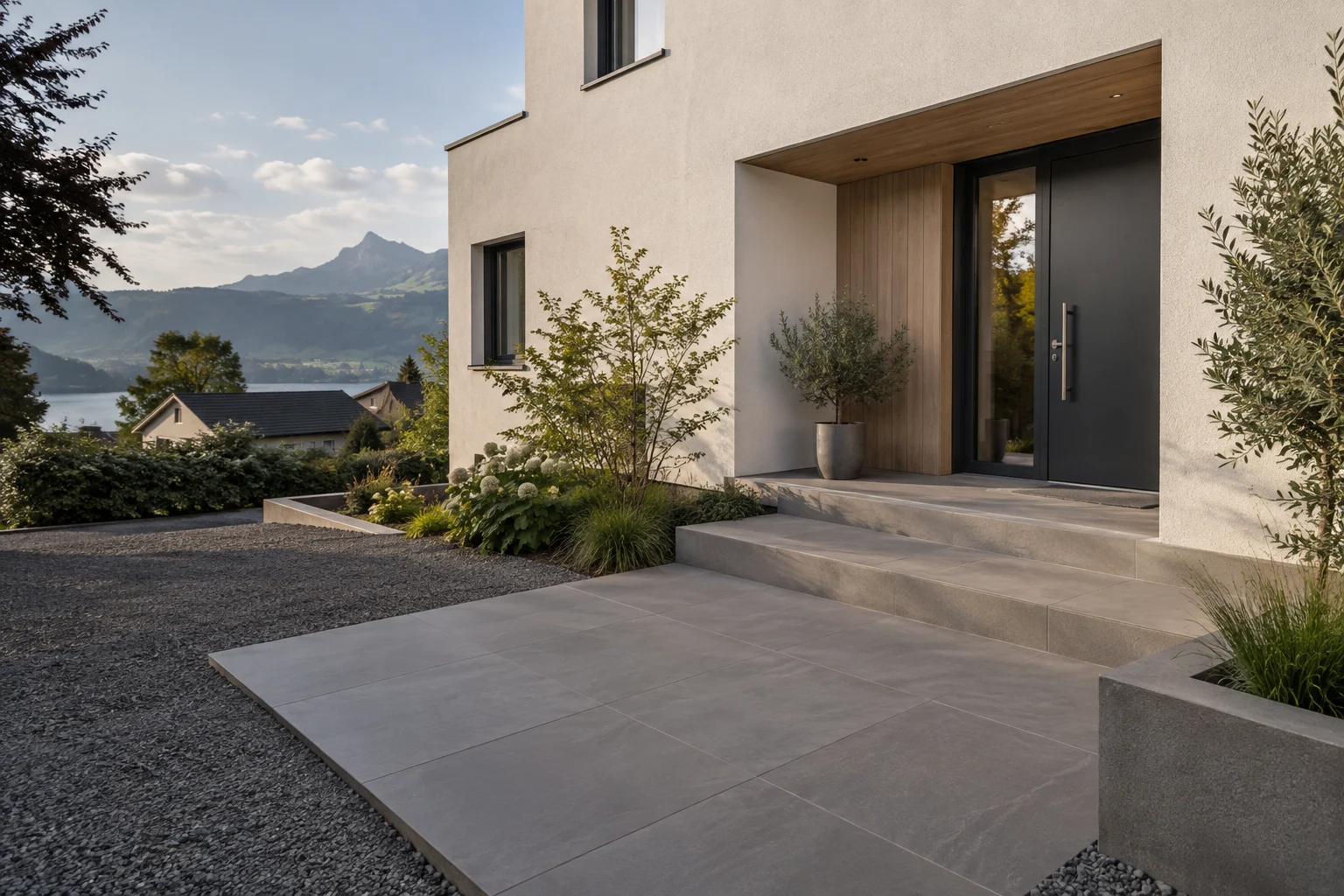 Helles Wohnhaus mit breiten Eingangsstufen, gestaltetem Aussenbereich und Blick auf See und Berge